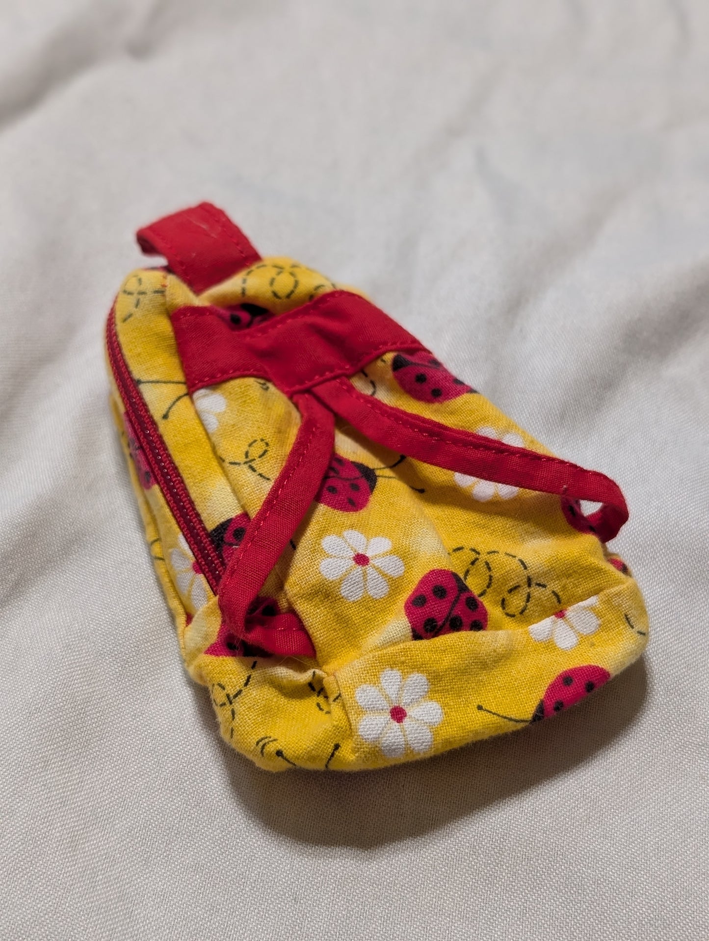 Yellow fabric pouch with red strap on a light gray background