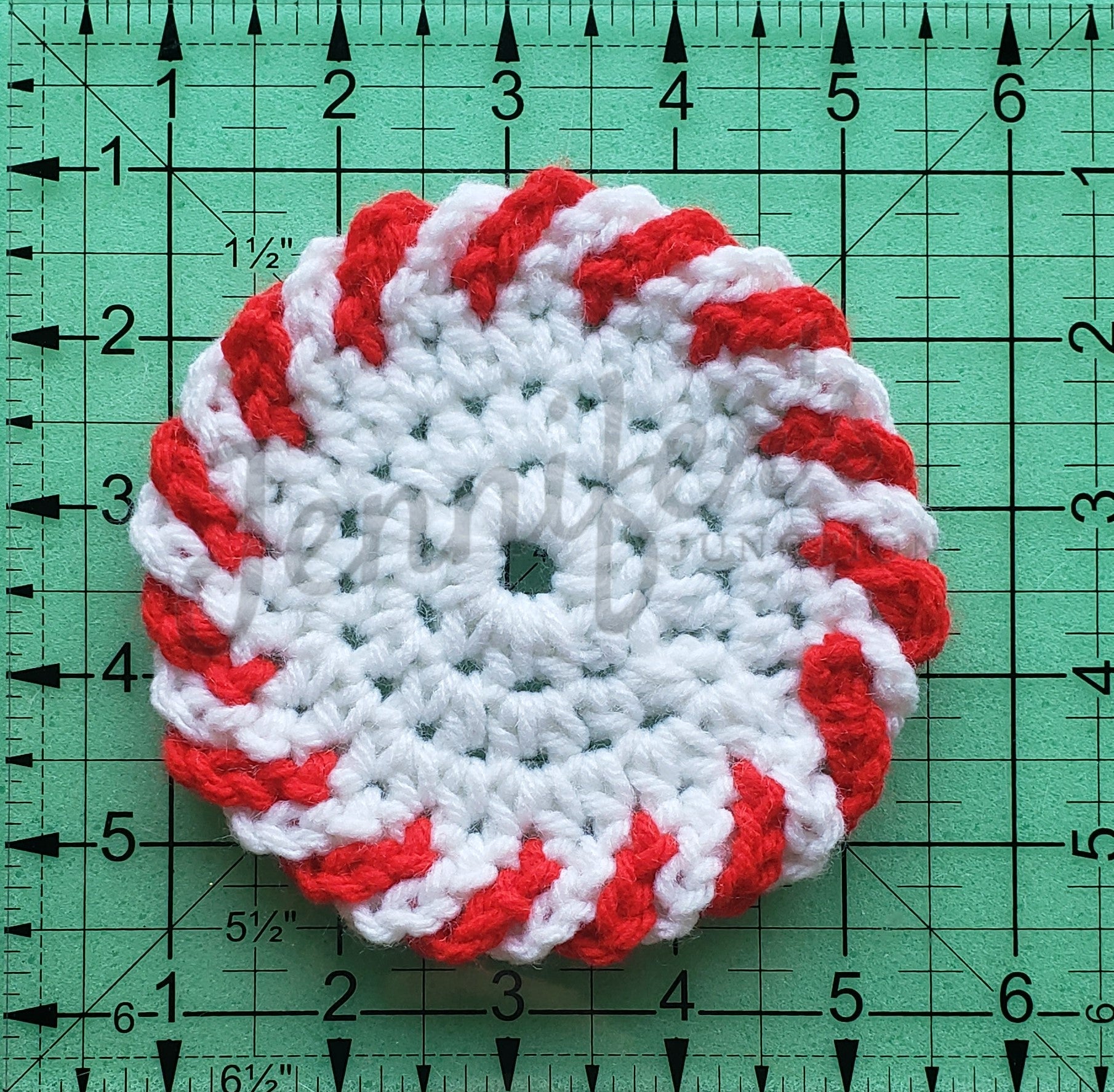 Crocheted peppermint candy coaster on a green cutting mat with measurements.